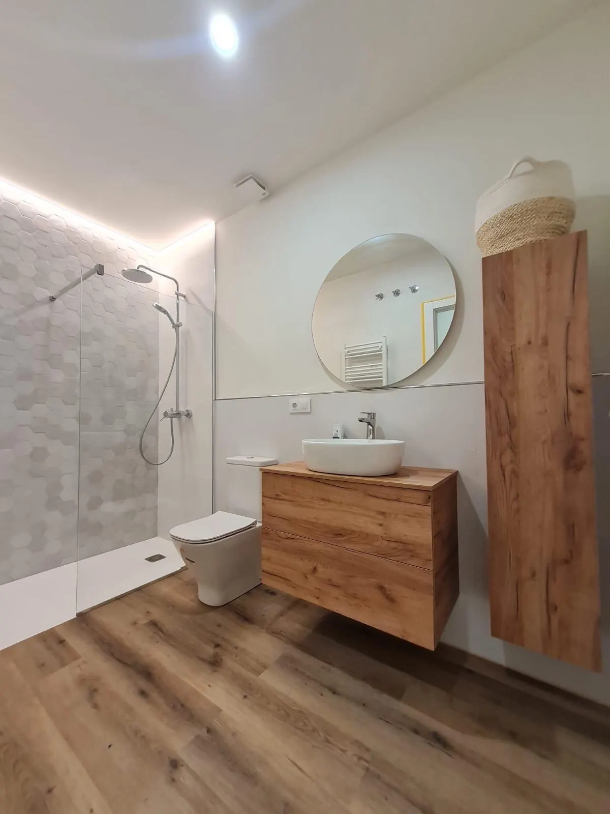 Baño reformado por Gasparini Construcciones, con mueble de madera, espejo redondo y ducha de obra